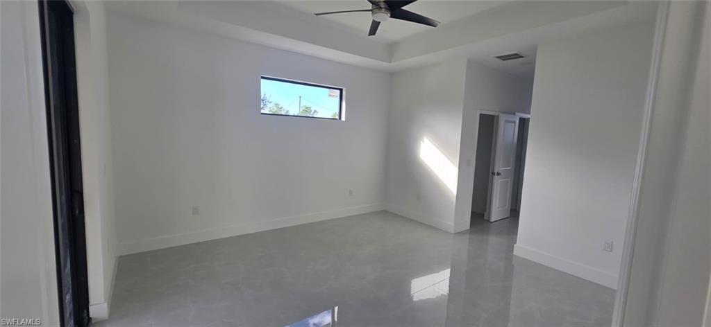Unfurnished room with finished concrete flooring, a raised ceiling, and ceiling fan