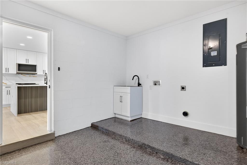 Laundry room with electric dryer hookup, electric panel, hookup for a washing machine, dark aggregate flooring, and water heater