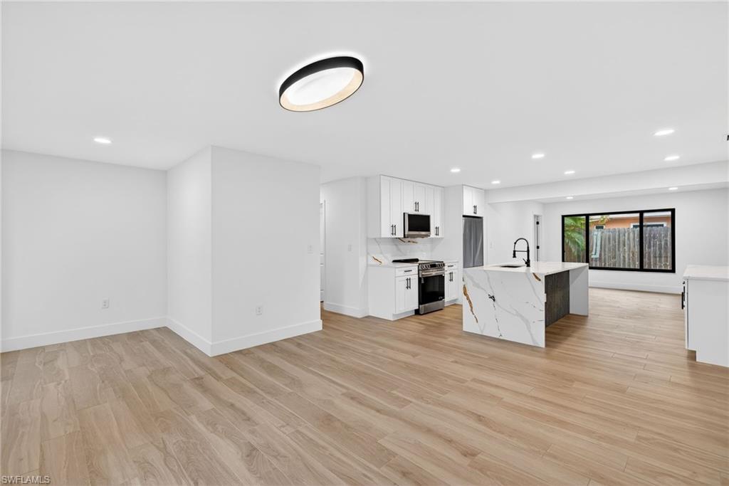 Kitchen featuring white cabinets, stainless steel appliances, light wood-style flooring, recessed lighting, and light stone counters