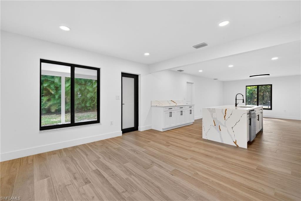 Kitchen with white cabinetry, light stone counters, light wood finished floors, recessed lighting, and an island with sink