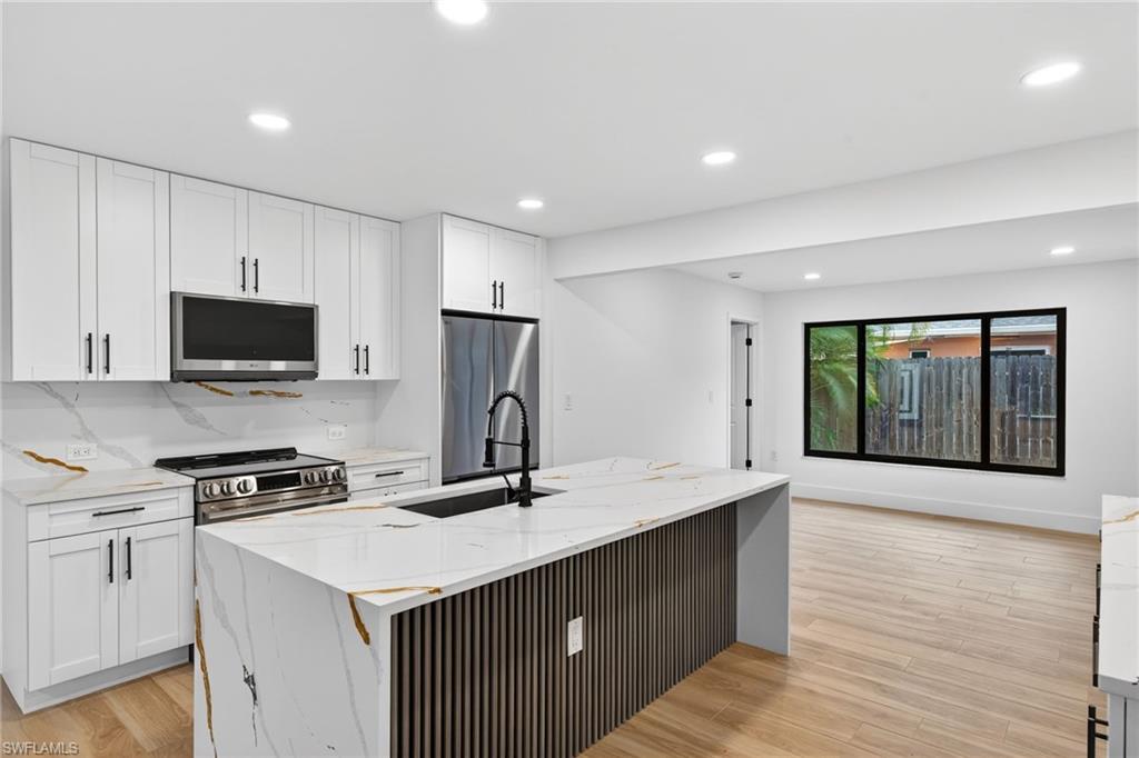 Kitchen with light stone counters, light wood-type flooring, white cabinets, recessed lighting, and appliances with stainless steel finishes