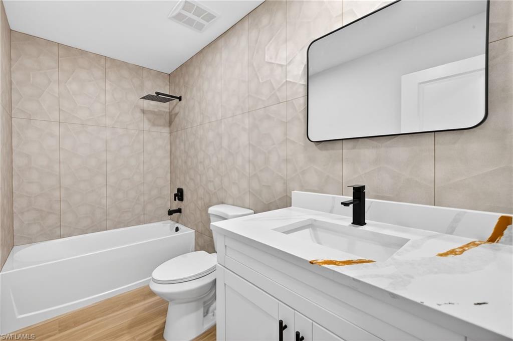 Bathroom with tile walls,  shower combination, vanity, and light wood-type flooring