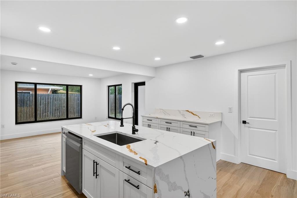 Kitchen with white cabinetry, light stone counters, recessed lighting, light wood-style floors, and a kitchen island with sink