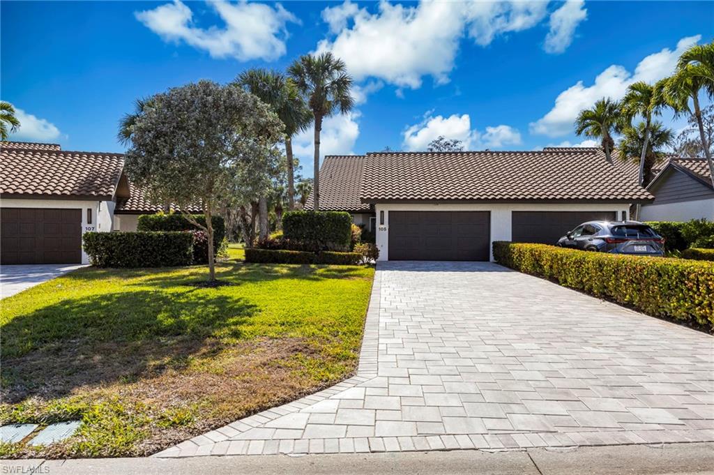 View of front of house featuring stucco siding, a tiled roof, decorative driveway, a front lawn, and an attached garage