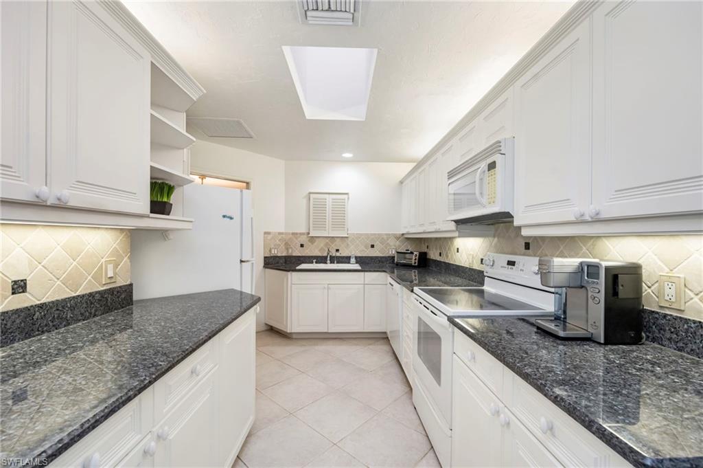 Kitchen featuring white appliances, open shelves, white cabinets, light tile patterned floors, and tasteful backsplash