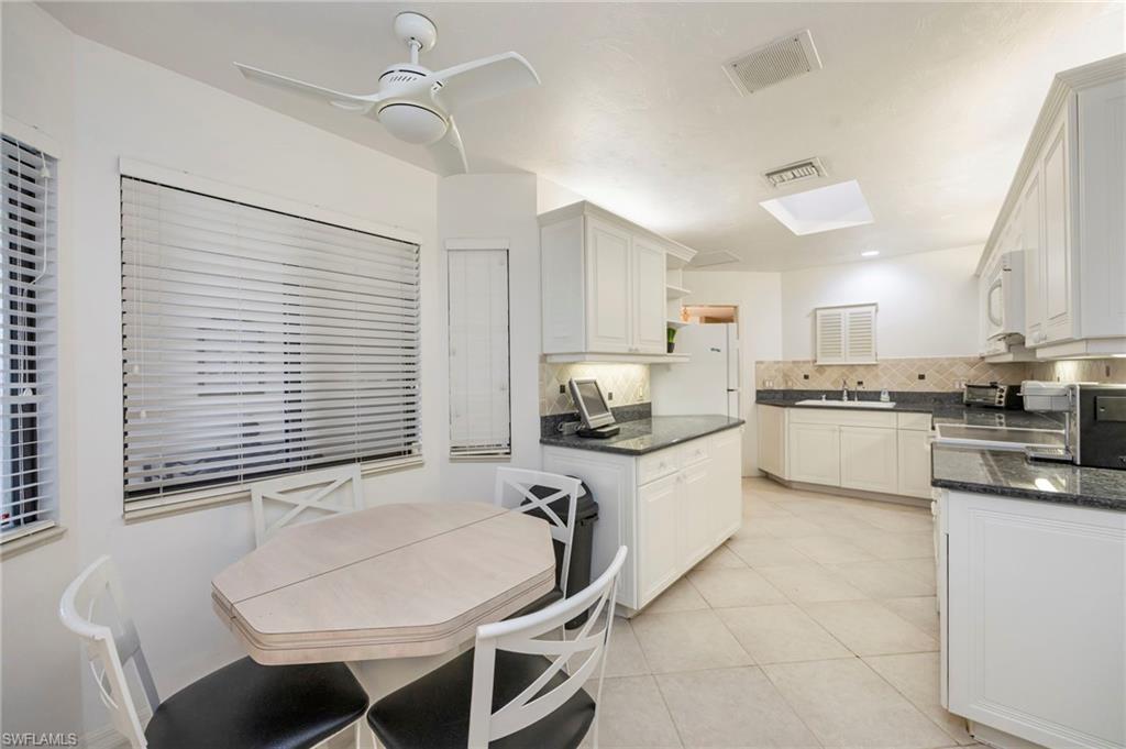 Kitchen featuring white cabinets, open shelves, dark stone counters, a ceiling fan, and white appliances