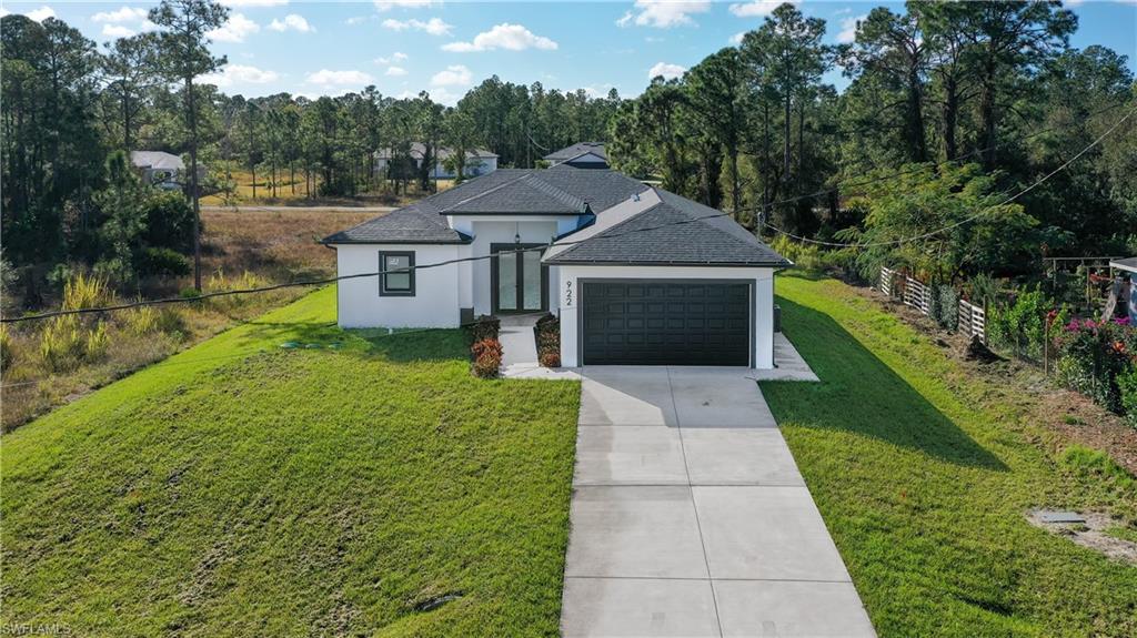 French country home with roof with shingles, concrete driveway, stucco siding, a garage, and view of wooded area