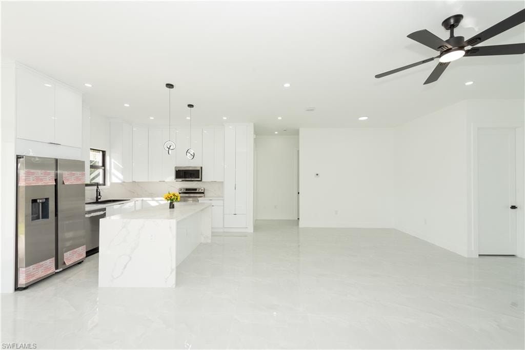 Kitchen featuring stainless steel appliances, decorative light fixtures, white cabinets, a center island, and light stone countertops