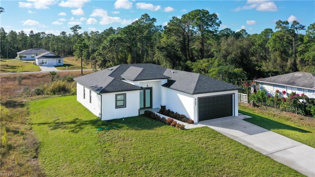View of front facade featuring roof with shingles, stucco siding, a front lawn, driveway, and an attached garage