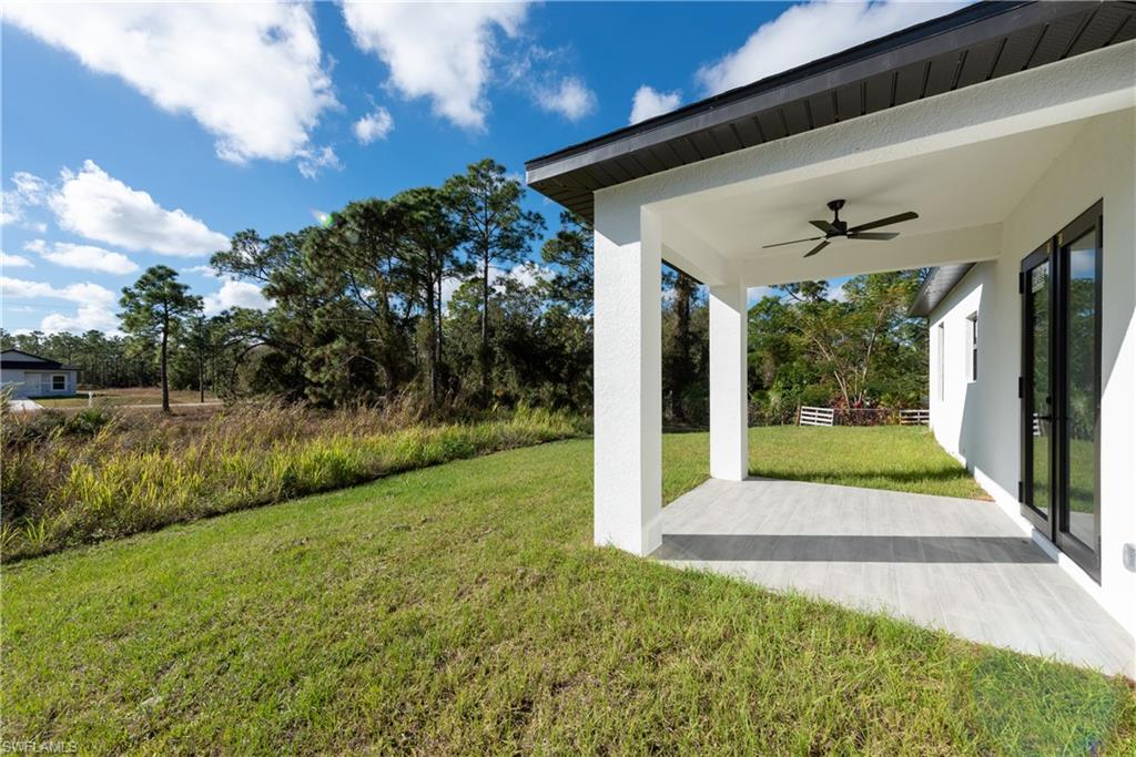 View of grassy yard featuring a ceiling fan, a patio area, and view of scattered trees