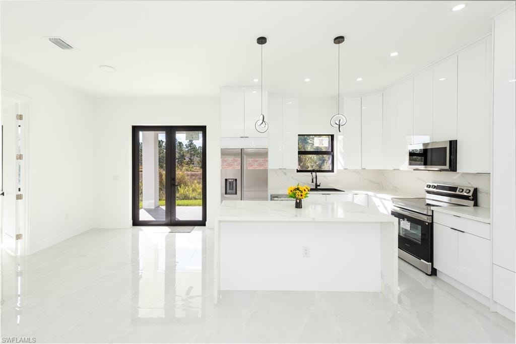 Kitchen featuring modern cabinets, a kitchen island, white cabinetry, stainless steel appliances, and recessed lighting