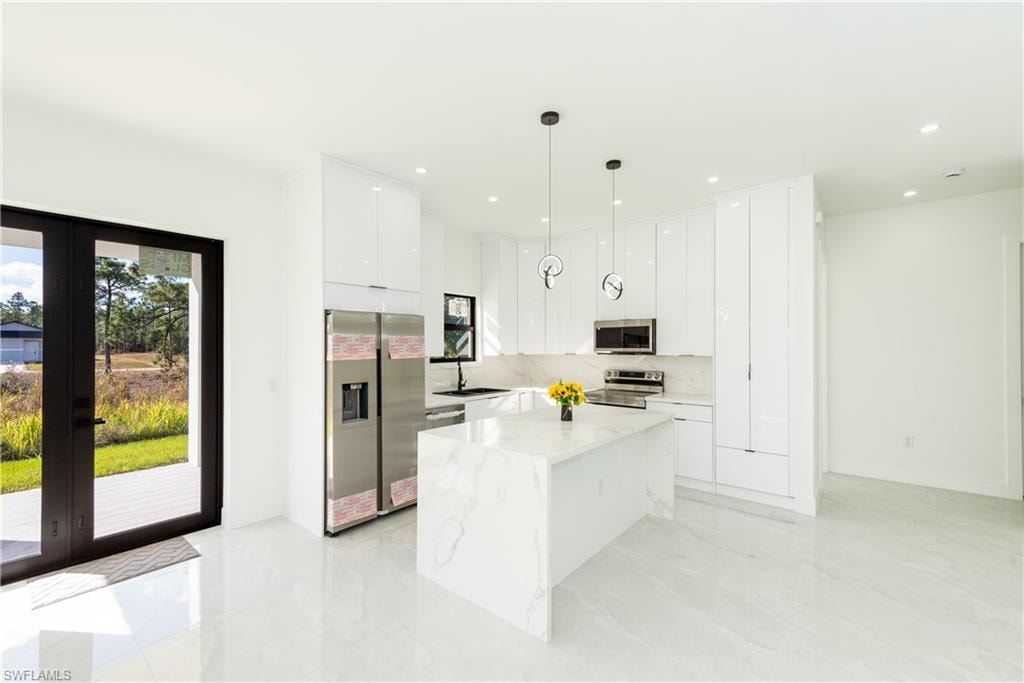 Kitchen featuring appliances with stainless steel finishes, french doors, white cabinetry, a kitchen island, and decorative light fixtures