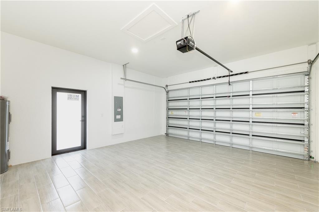 Garage featuring electric panel, a garage door opener, and water heater