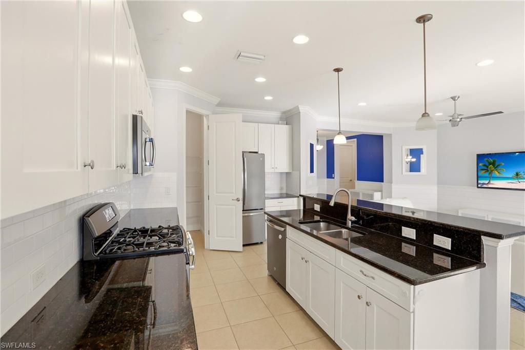 Kitchen featuring white cabinets, dark stone counters, backsplash, stainless steel appliances, and a kitchen island with sink
