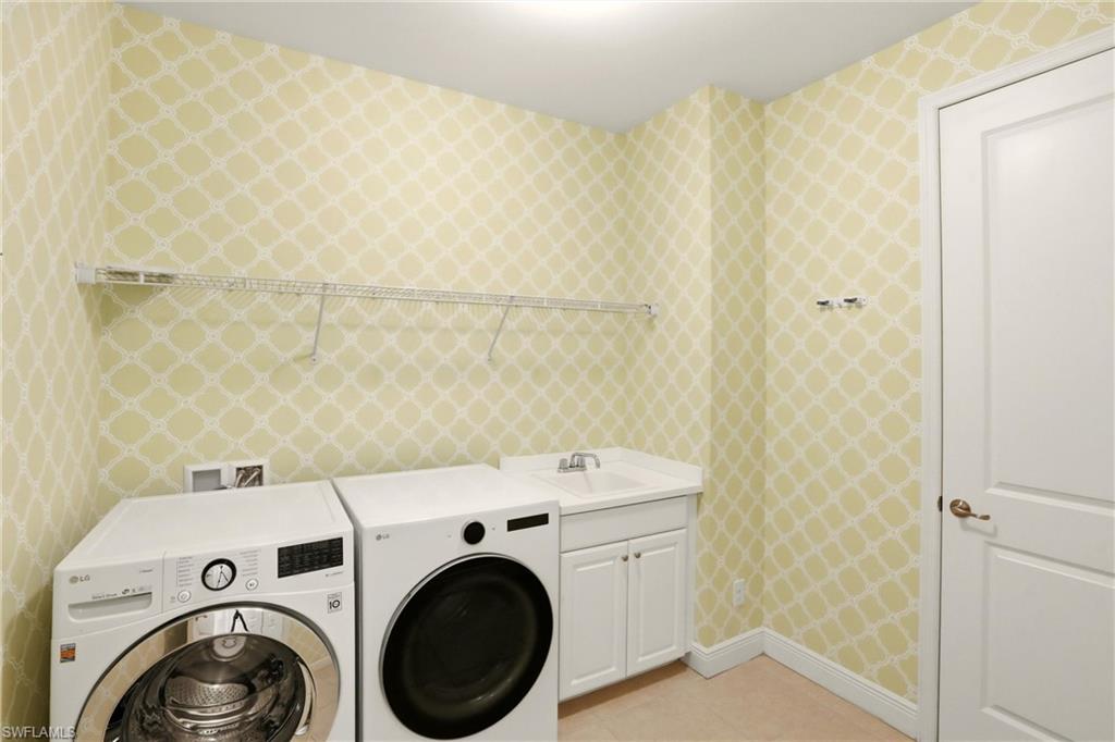 Laundry room featuring wallpapered walls, separate washer and dryer, light tile patterned flooring, and cabinet space