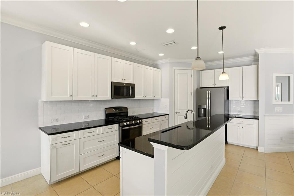 Kitchen featuring white cabinetry, pendant lighting, stainless steel appliances, light tile patterned flooring, and ornamental molding