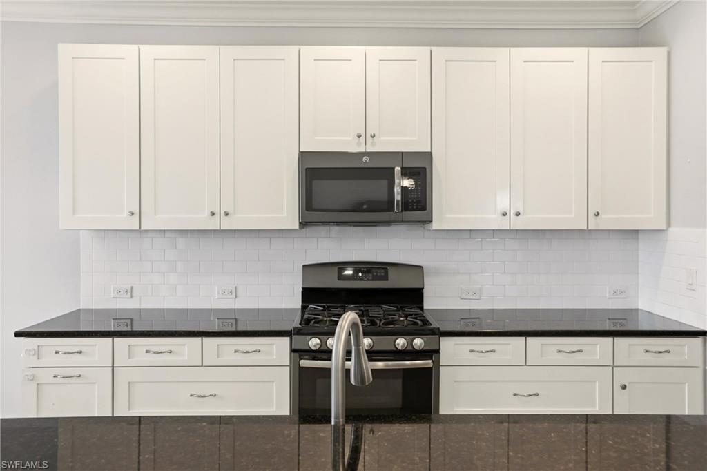 Kitchen featuring gas range oven, stainless steel microwave, white cabinetry, and dark stone counters