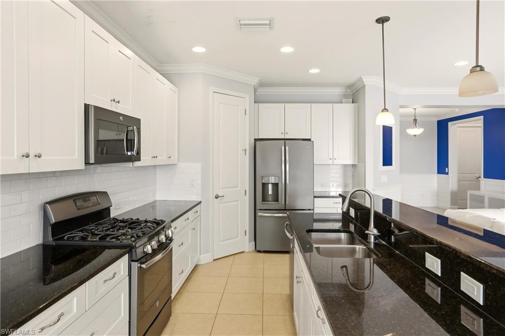 Kitchen featuring appliances with stainless steel finishes, dark stone counters, white cabinetry, decorative backsplash, and crown molding
