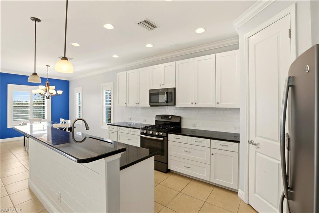 Kitchen featuring white cabinets, stainless steel appliances, a kitchen island with sink, decorative light fixtures, and decorative backsplash