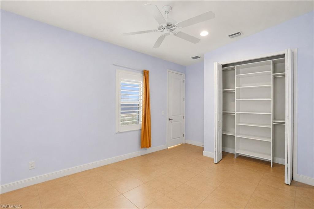 Room featuring tile flooring, a built-in closet with shelving and hanging rods, a window with plantation shutters, a ceiling fan, and recessed lighting
