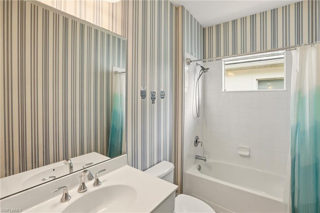 Bathroom featuring wallpapered walls, shower / tub combo, and vanity