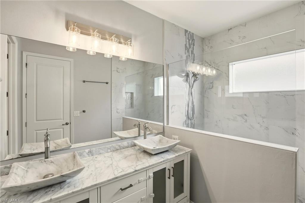 Bathroom with a marble finish shower, double vanity, and plenty of natural light