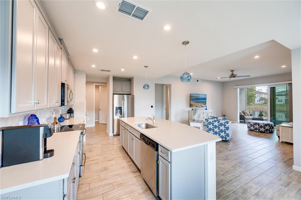 Kitchen with decorative light fixtures, open floor plan, wood-look tile floors, a kitchen island with sink, and a ceiling fan
