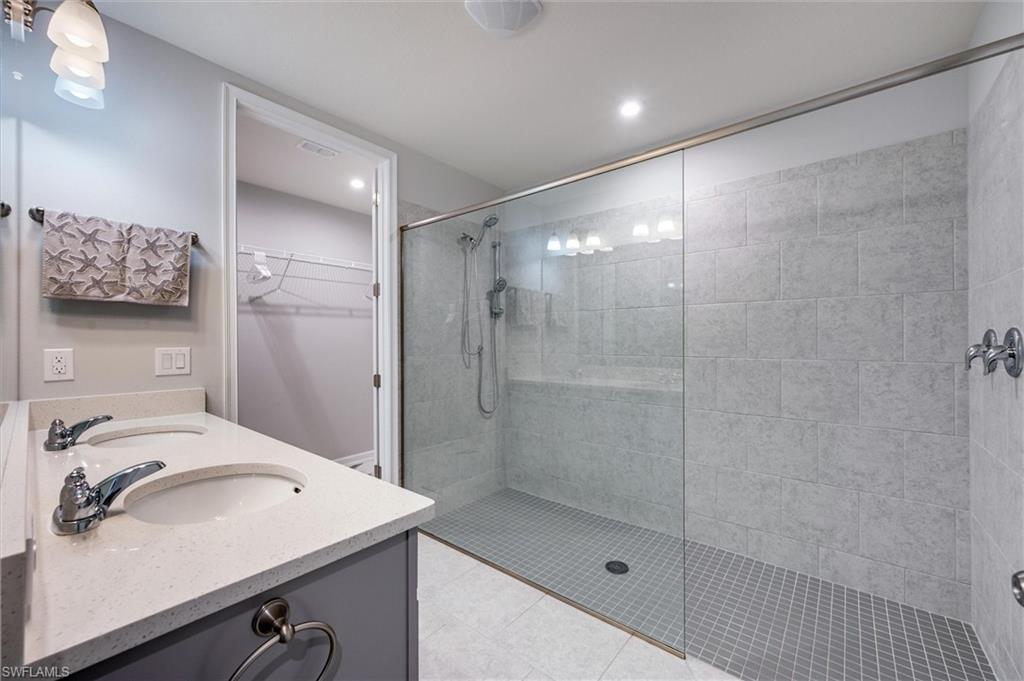 Primary bath featuring a spacious closet, a walk in shower, double vanity, and light tile patterned floors