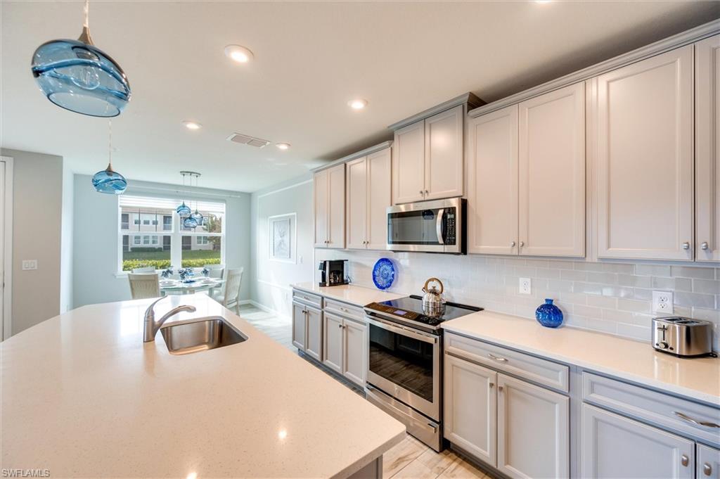 Kitchen featuring appliances with stainless steel finishes, hanging light fixtures, a kitchen island with sink, recessed lighting, and light stone countertops