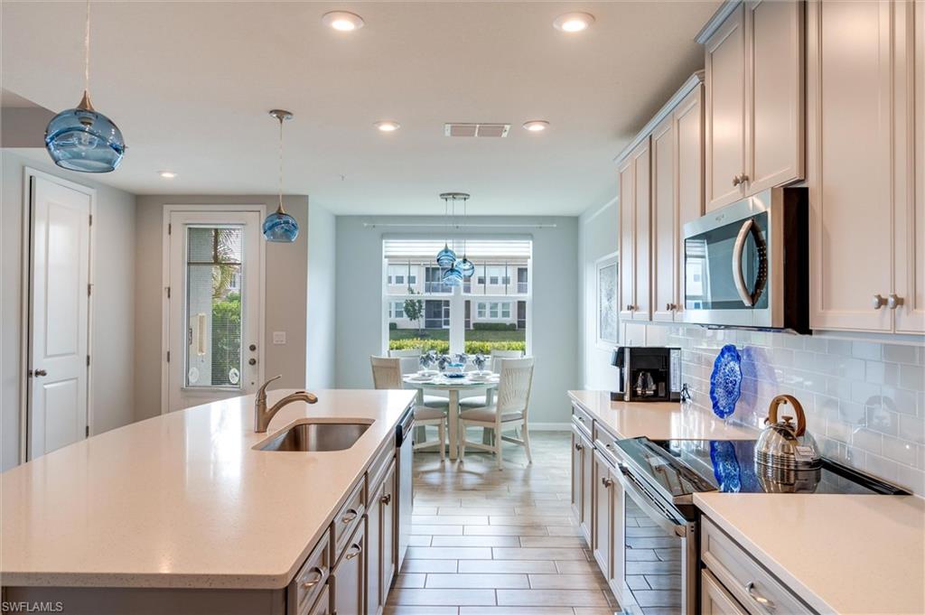 Kitchen with stainless steel appliances, decorative light fixtures, a kitchen island with sink, light stone counters, and recessed lighting