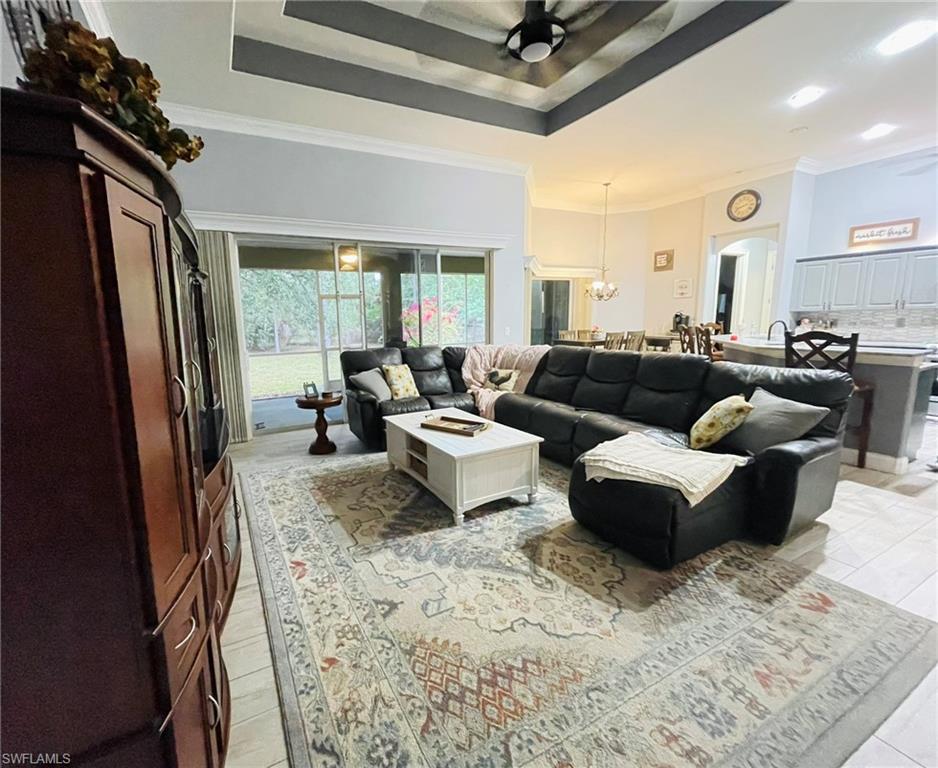 Living area featuring a raised ceiling, ceiling fan, ornamental molding, a chandelier, and arched walkways