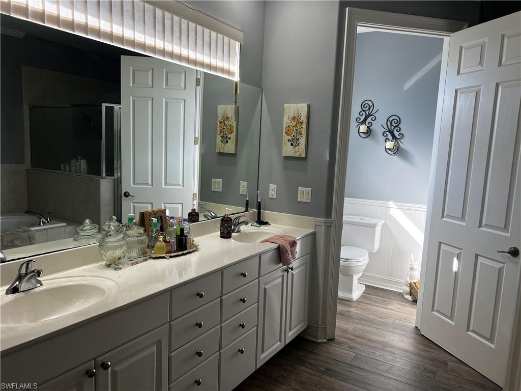 Bathroom with a bath, a shower stall, double vanity, dark wood-style flooring, and a wainscoted wall