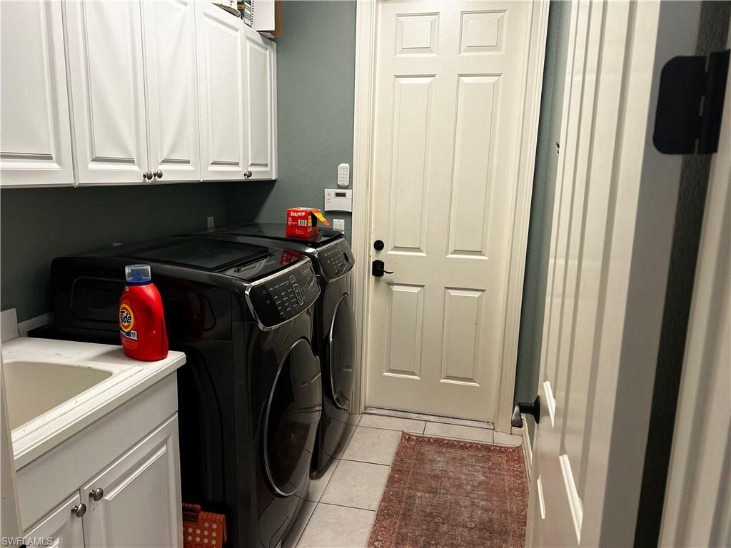 Laundry room with separate washer and dryer, light tile patterned flooring, and cabinet space