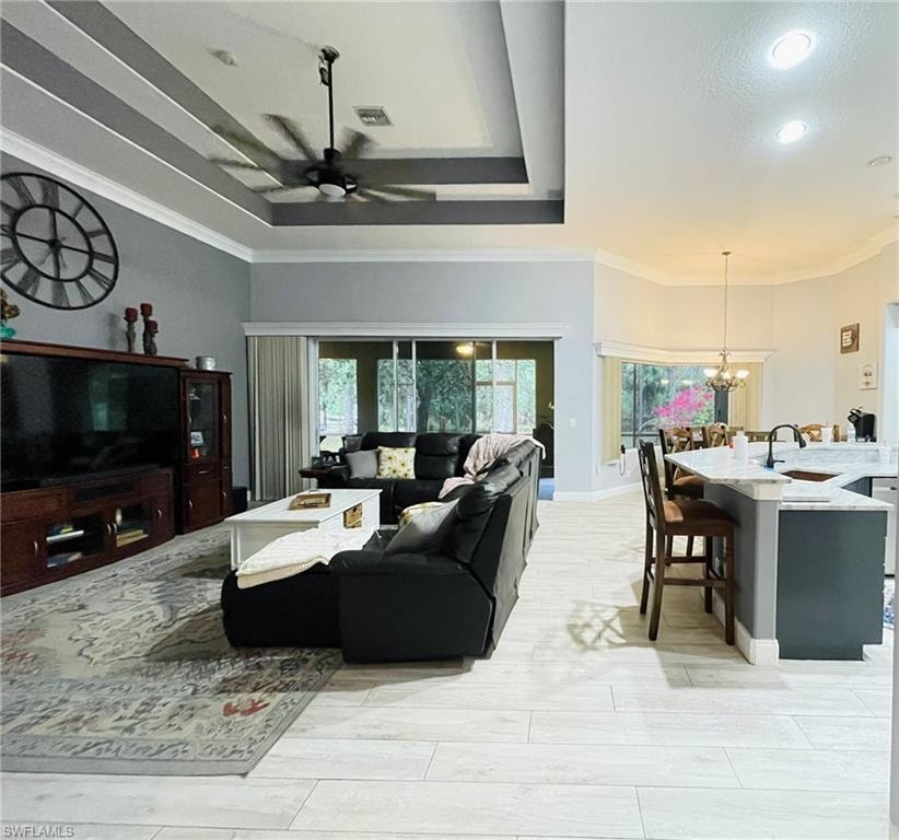 Living area featuring a chandelier, crown molding, a ceiling fan, and a raised ceiling