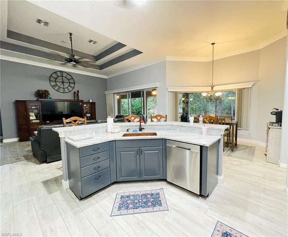 Kitchen featuring a kitchen island with sink, dishwasher, crown molding, light stone countertops, and open floor plan
