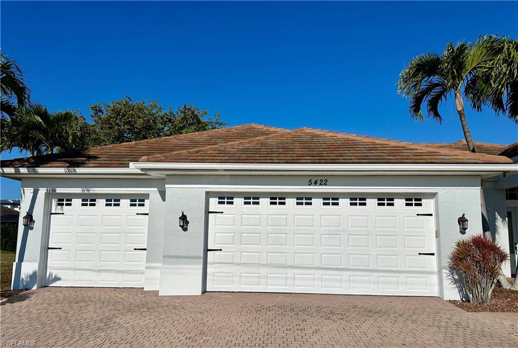View of Newly Painted Three Car Garage with Three Car Paver Driveway and Exterior Outdoor Garage Sconce Illumination.