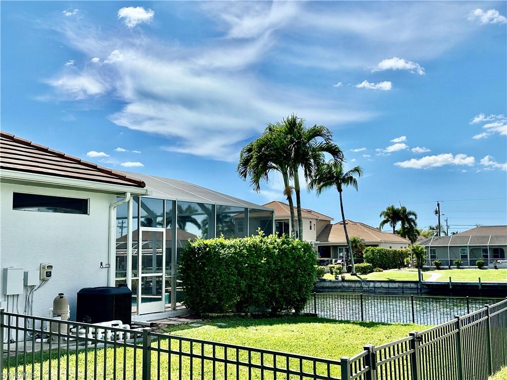 View of the iron fencing around the property, the lanai's outdoor kitchen dormer window, the side of the pool equipment and pool heater and the screendoor into screen enclosed pool facing the Gulf access canal.
