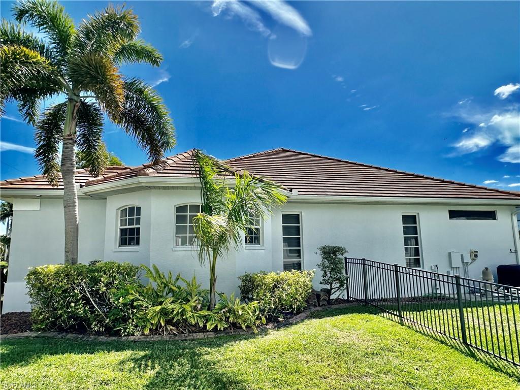 View of the newly painted home's Primary Suite's large bath's WALK IN SHOWER windows, the two SIDE by SIDE Primary Suite Bedroom Plantation Shuttered Windows, the above Outdoor Kitchen/Lanai Dormer Window and the Iron Fencing surrounding the property with view of the Pool Equipment/Pool Heater and again Designed Garden.