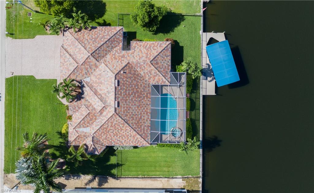 The Aerial View of the newly painted home with its design of numerous beautiful property palms, with screened pool cage and covered boat lift on the Gulf access canal.