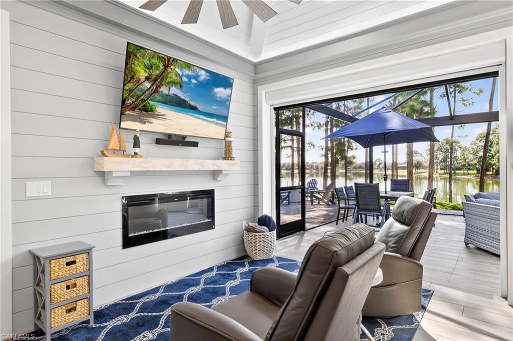 Living area with a sunroom, plenty of natural light, a glass covered fireplace, a ceiling fan, and wooden walls