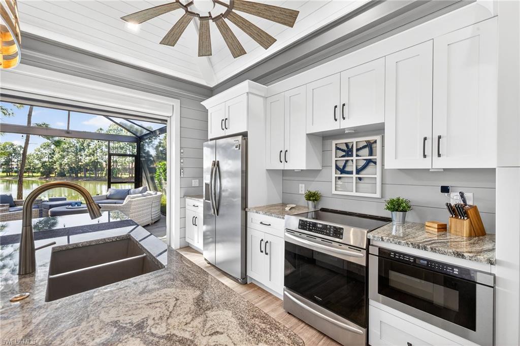 Kitchen featuring appliances with stainless steel finishes, light stone countertops, white cabinets, and wooden walls