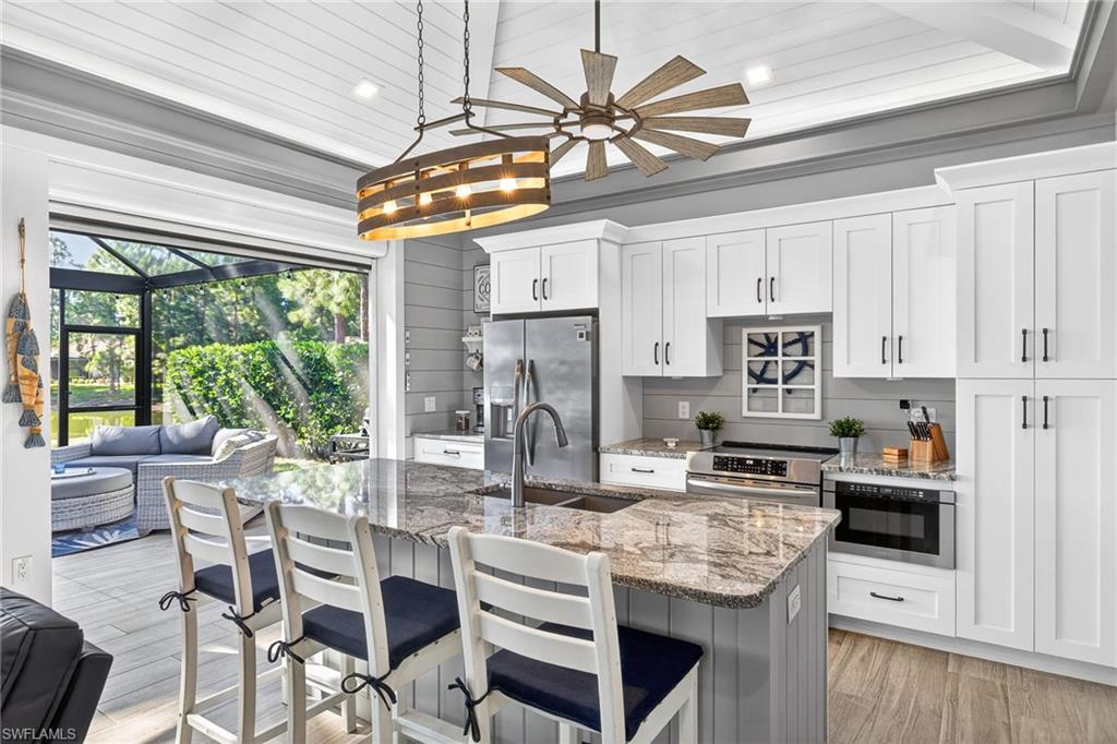 Kitchen featuring light stone counters, stainless steel appliances, a kitchen breakfast bar, light wood-type flooring, and white cabinetry