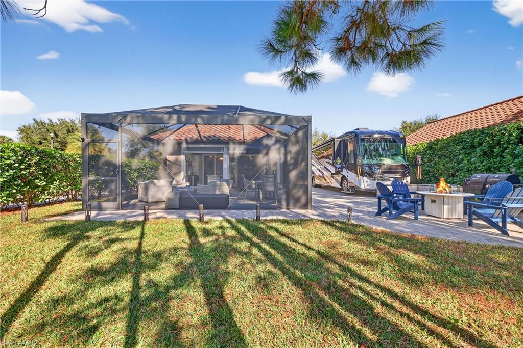 Back of house featuring a lawn, a patio, an outdoor fire pit, glass enclosure, and a sunroom