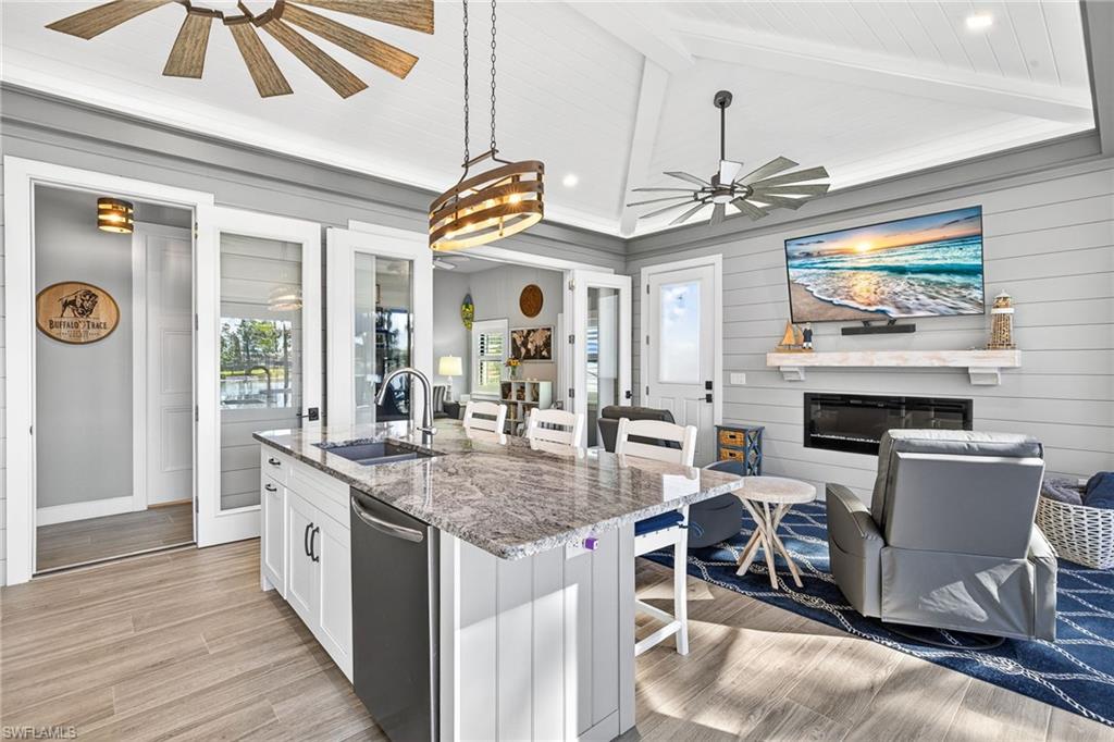 Kitchen featuring a breakfast bar, light stone counters, white cabinetry, an island with sink, and light wood-type flooring