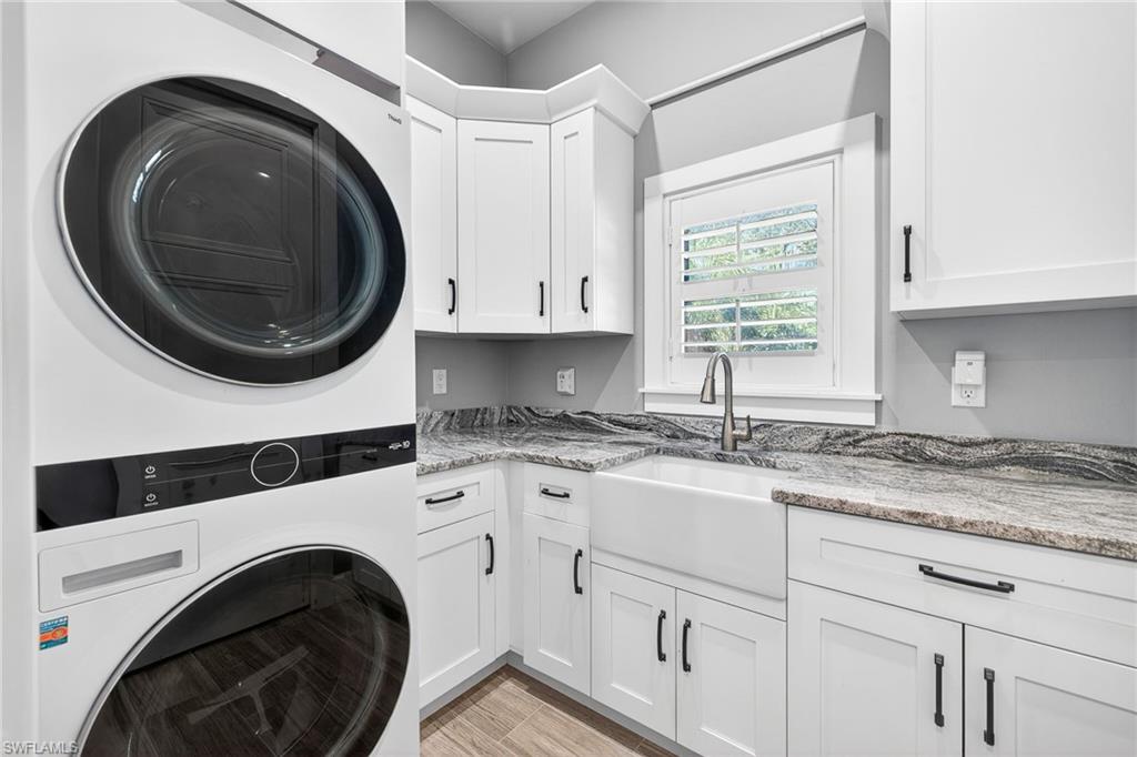 Laundry area with estacked washer and dryer, cabinet space, and light wood-style floors
