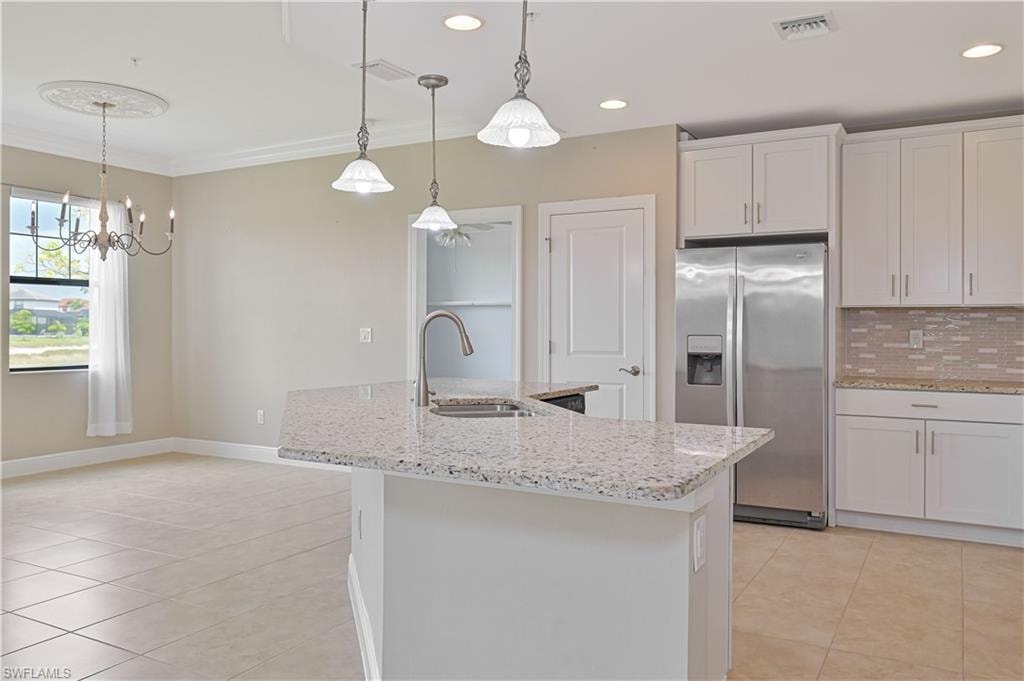 Kitchen island with stone countertop, stainless steel appliances, white cabinetry, tile backsplash, and recessed lighting