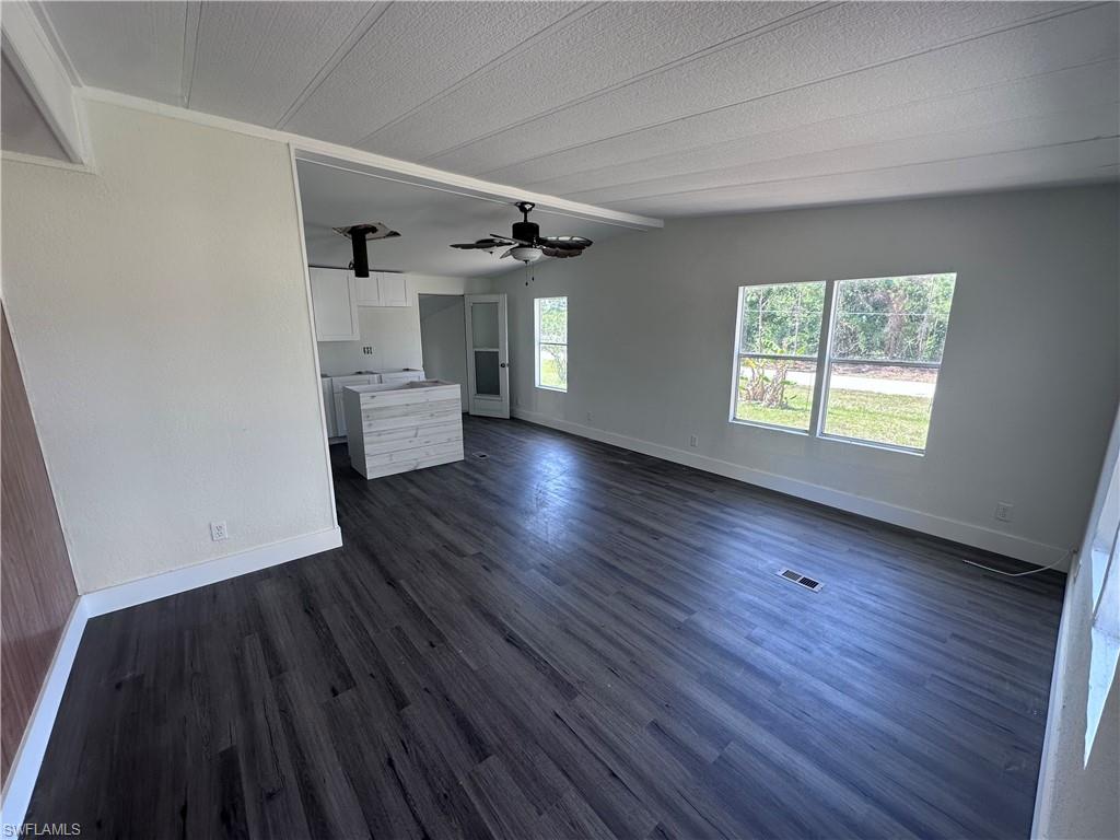 Unfurnished living room featuring dark wood finished floors, a textured ceiling, and ceiling fan