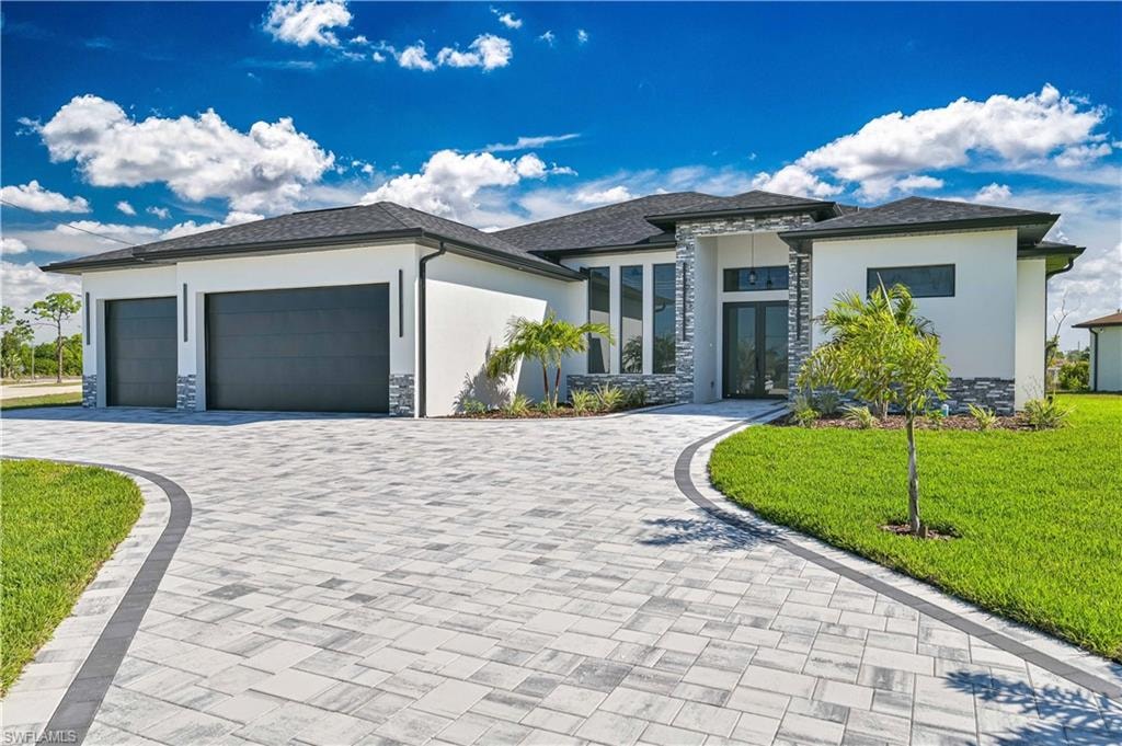 Prairie-style home featuring stone siding, a front lawn, a garage, decorative driveway, and stucco siding