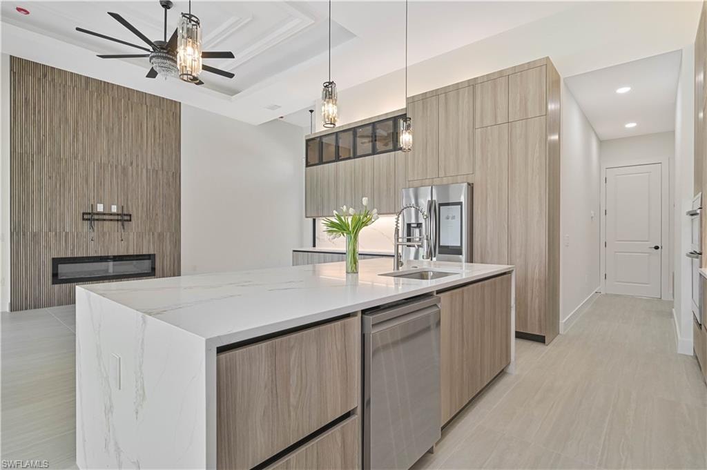 Kitchen featuring modern cabinets, light wood finish cabinetry, a kitchen island with sink, light stone countertops, and pendant lighting
