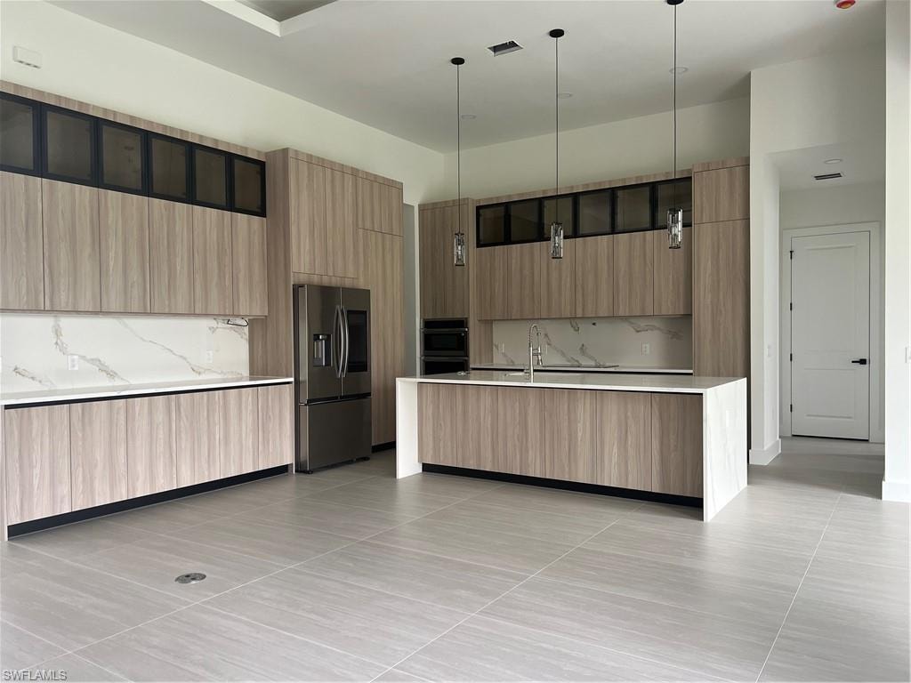 Kitchen featuring a kitchen island with sink, modern cabinets, decorative light fixtures, refrigerator, and decorative backsplash